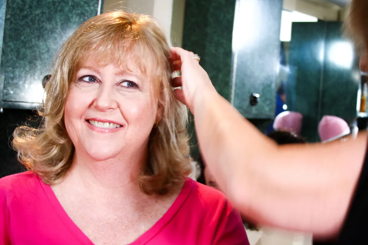 Stylist's hand working through a client's new blonde hair during a fitting, both reflected in the studio mirror