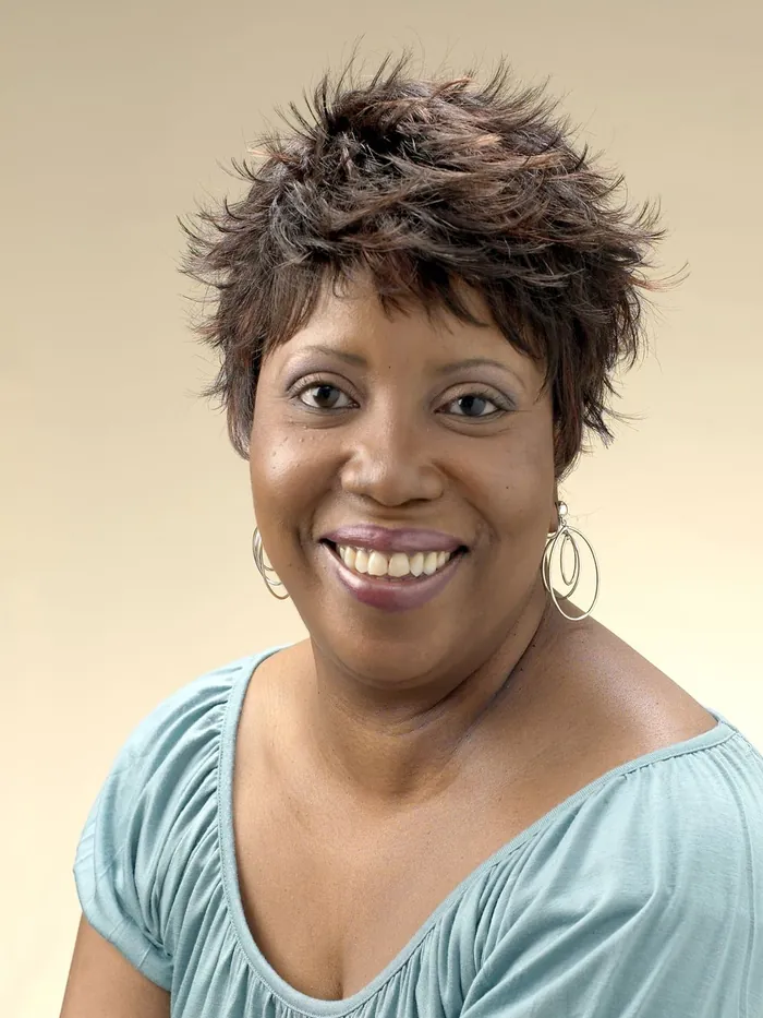 Studio portrait of a client with a full short textured style, smiling against a warm background
