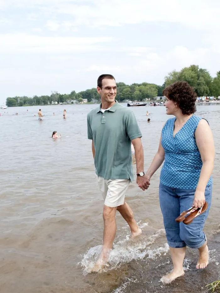 A couple walking hand in hand through ankle deep water at a lake beach