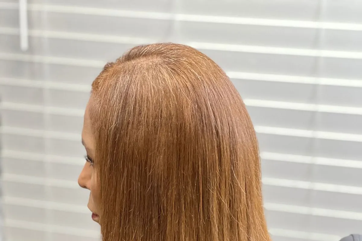 Long golden blonde hair falling over a styling cape, lit from the side to show condition along the full length