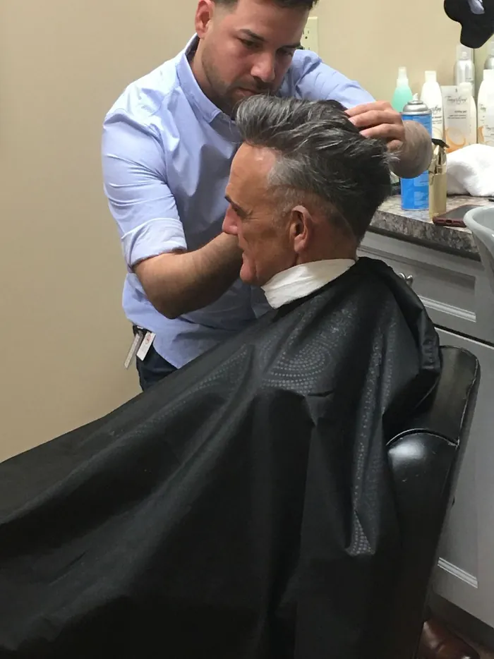 Specialist working on a seated client's hair system at a studio station with products on the counter