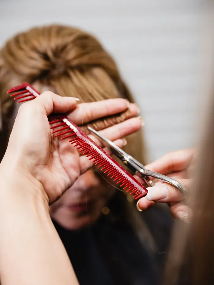 Two hands holding a cutting comb and shears against sectioned blonde hair during a trim