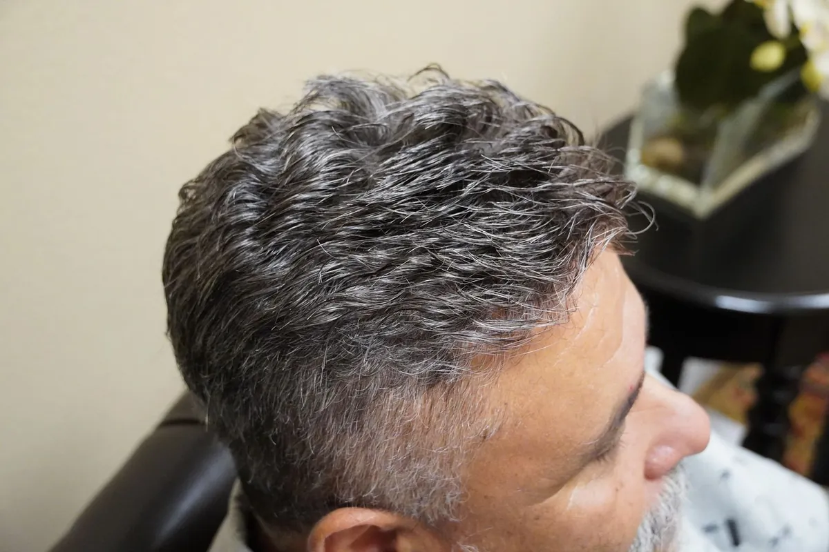 Side view close-up of a salt and pepper hair system showing the temple and sideburn blending into the existing hair