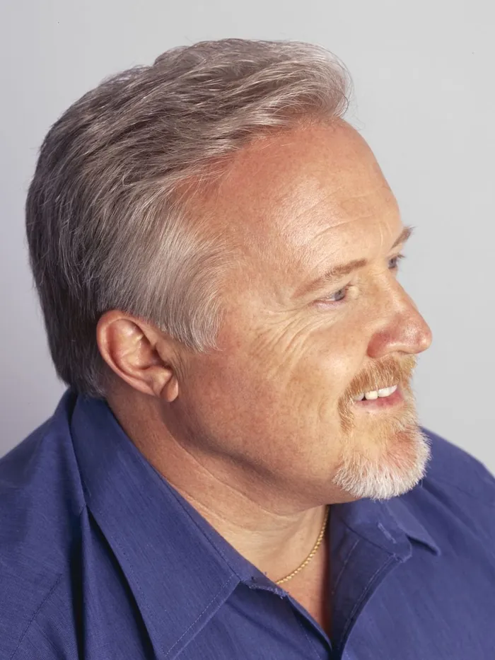 After: a full gray hair system in three-quarter profile, same blue shirt and same light gray backdrop
