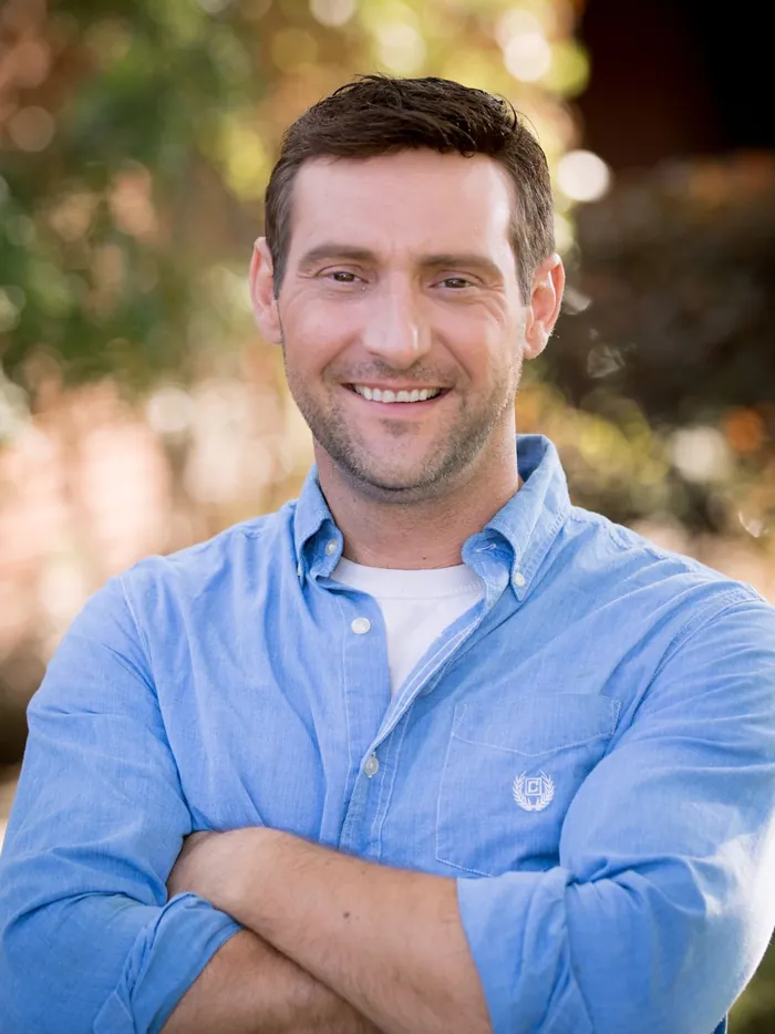 Man outdoors with a natural, undetectable custom hair replacement system, arms crossed and smiling