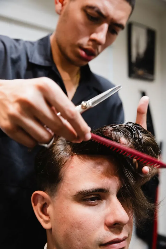 Specialist cutting a new hair replacement system into shape with scissors and a comb while the client sits in a cape