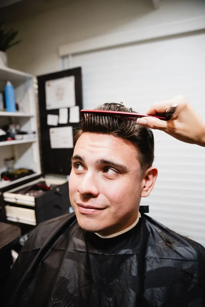 Finished hair replacement system being combed into place on a relaxed client in a salon chair