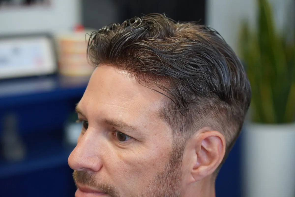 Side profile close-up showing the temple of a hair replacement system tapering into the client's own faded sides
