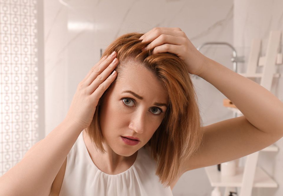Picture of a woman looking at herself in the mirror. She is touching her hair and examining her hairline, as if to look for signs of hair loss.